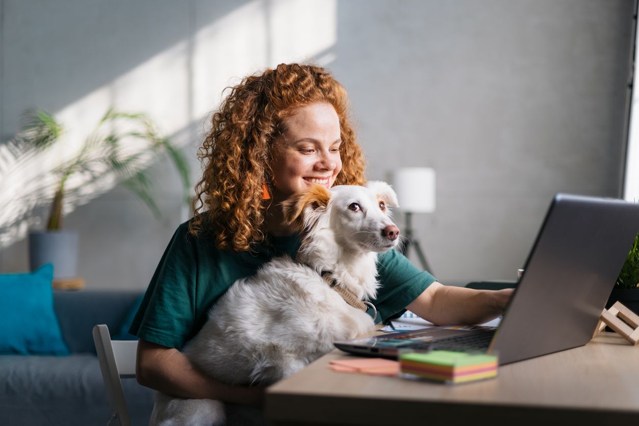 A dog owner and her dog sit in front of a laptop in a well-lit room