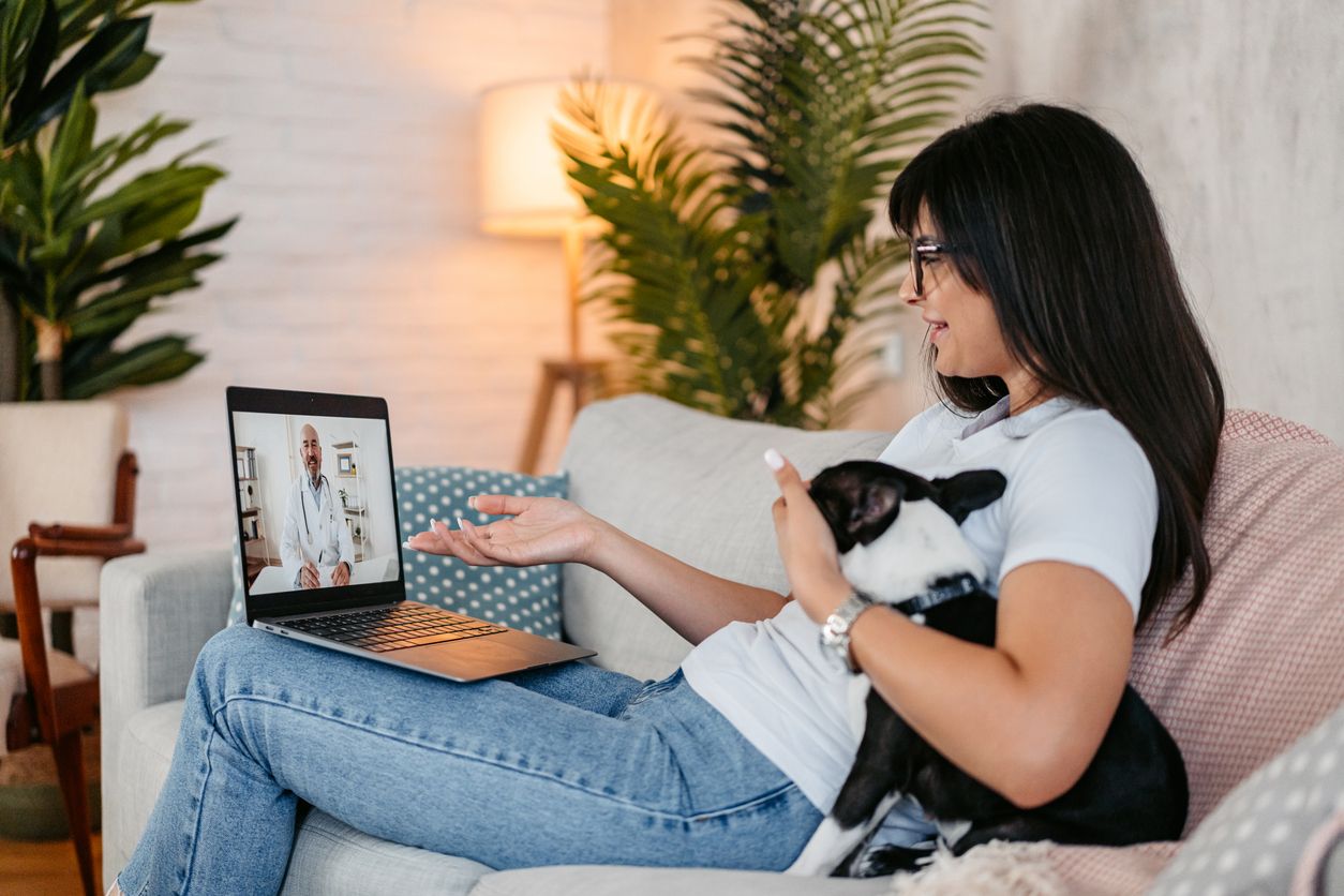 A woman sits with her dog on a virtual vet appointment