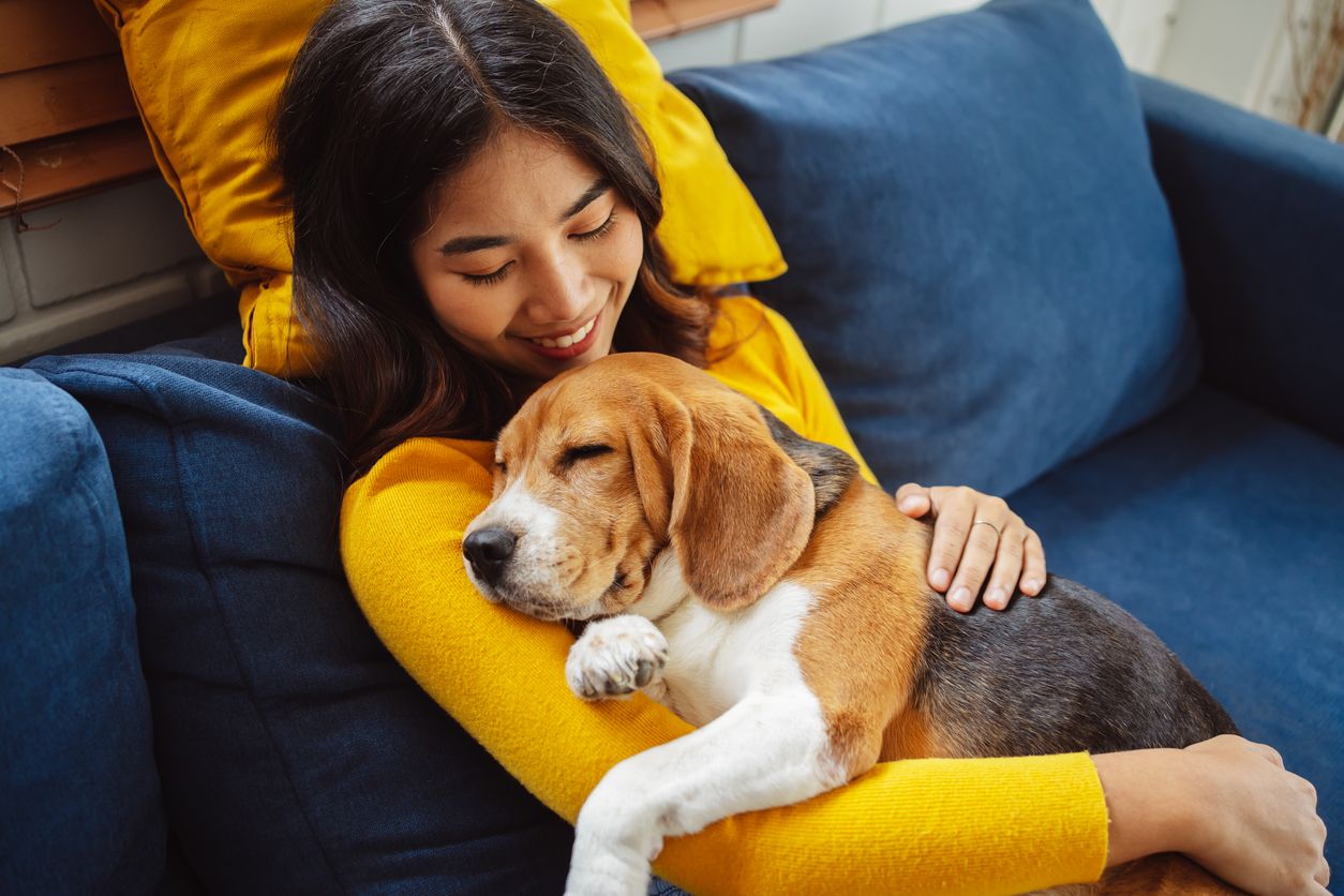 A smiling woman hugging a dog while sitting on a couch.